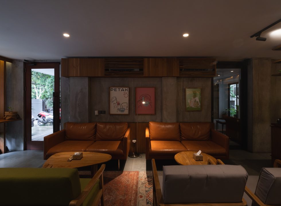 Ruang tamu PETAK 25 dengan dua sofa kulit cognac dan tiga karya seni berbingkai di dinding belakang